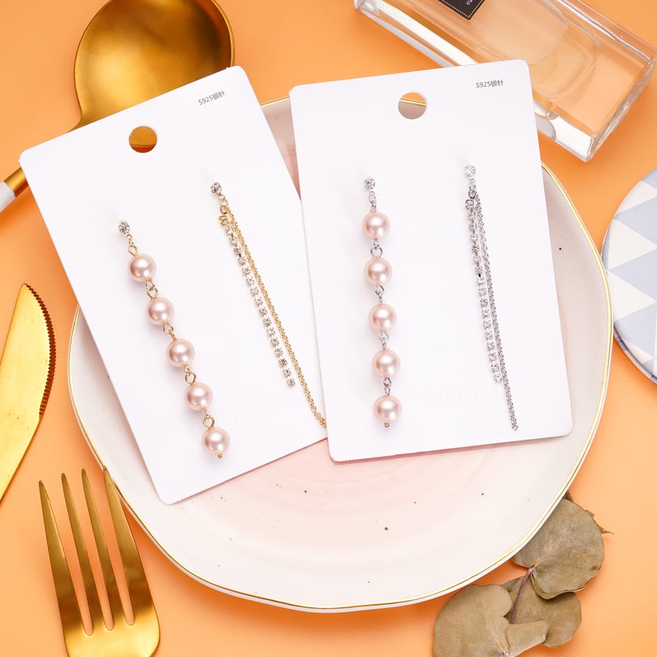 Pares de aretes largos asimétricos en tonos dorado y plateado sobre sus tarjetas de exhibición