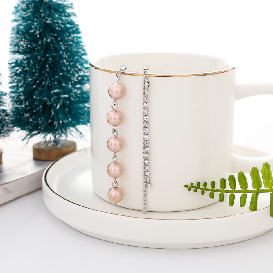 Aretes asimétricos plateados con perlas rosadas colgando de una taza