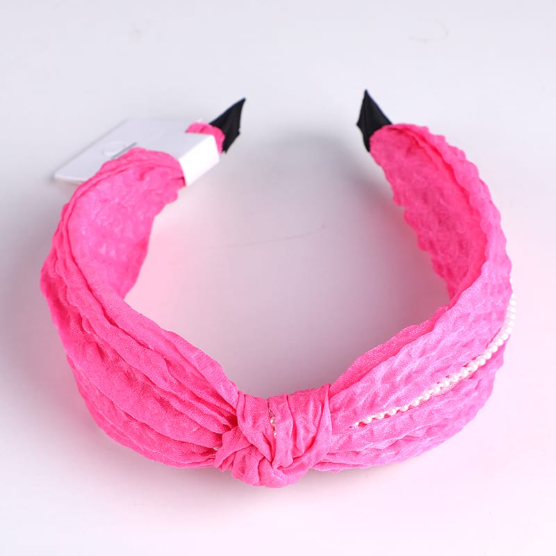 Diadema fucsia con nudo y detalle de perlas sobre fondo blanco