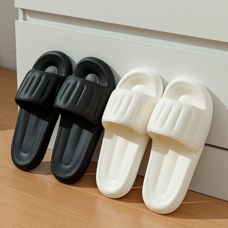 Par de pantuflas negras y par de pantuflas beige con textura acanalada apoyadas en la pared
