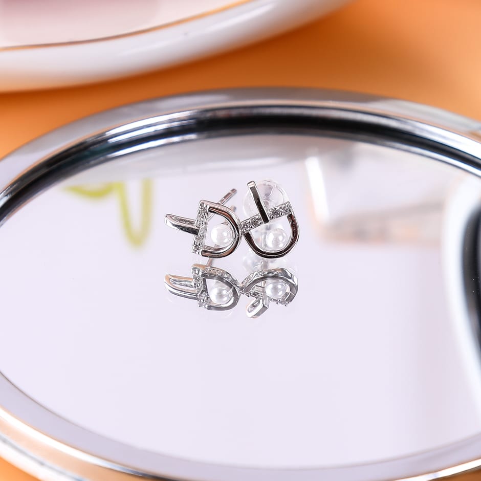 Par de aretes plateados con detalle de perla reflejados en un espejo de mano