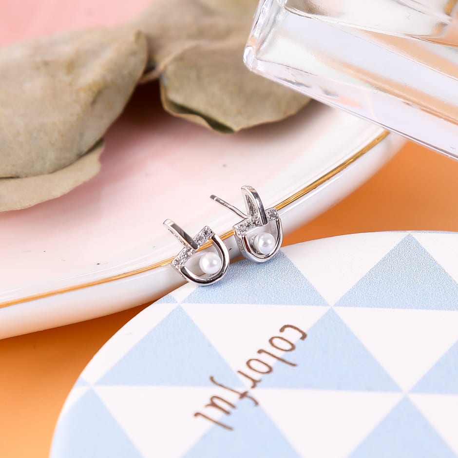 Aretes plateados con forma de arco y perla sobre un plato decorativo