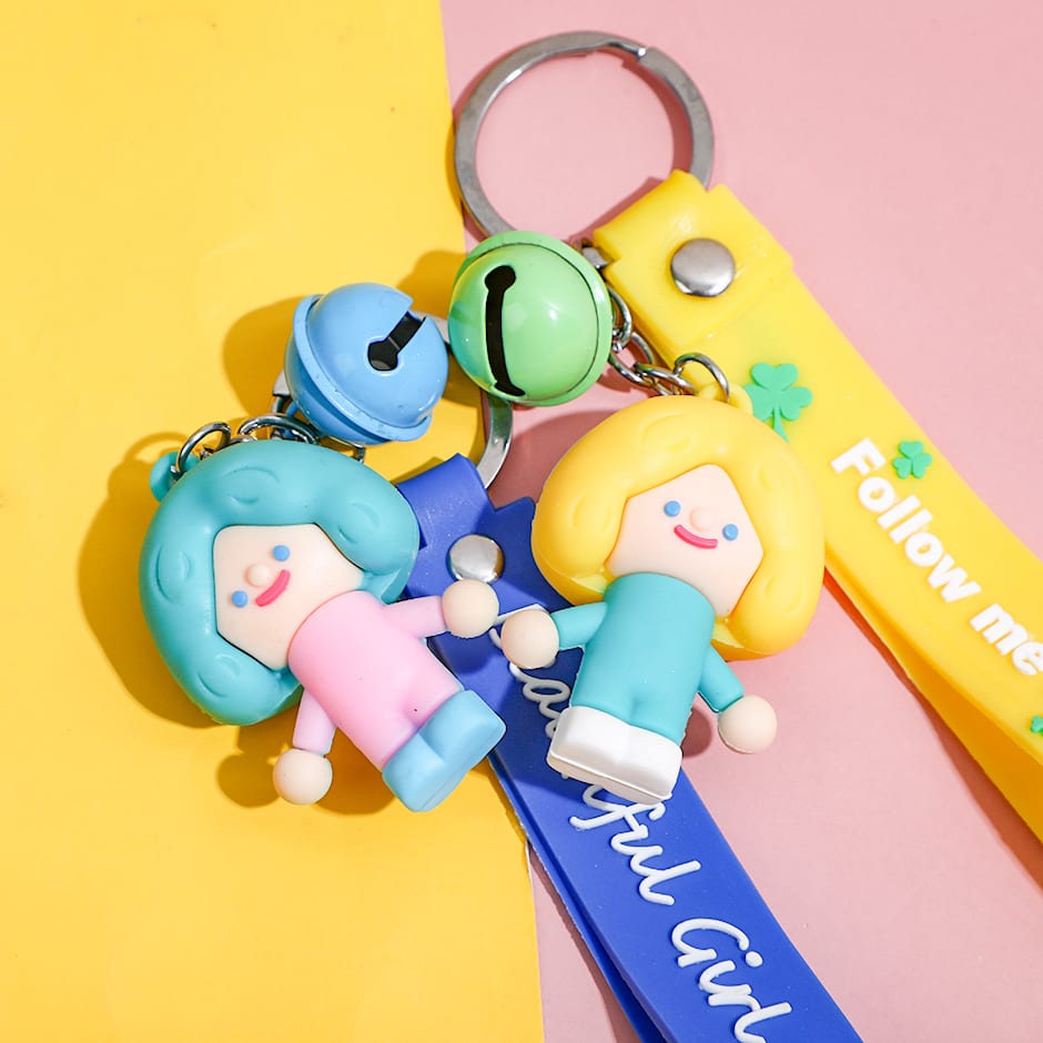 Primer plano de los llaveros con figuras de muñeca en tonos pastel, cascabel redondo y correas estampadas