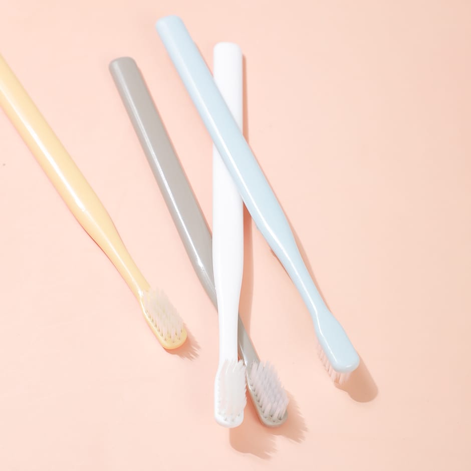 Cuatro cepillos de dientes con cabezal compacto y mangos rectos en colores amarillo, gris, blanco y celeste